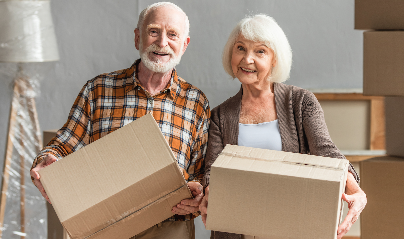 Ein älteres Paar hält zwei Umzugskartons in einer Innenumgebung mit Umzugsmaterialien.